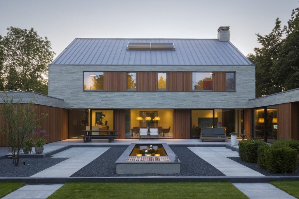 Moderne villa met grote ramen en strakke lijnen in een tuin met waterpartij.