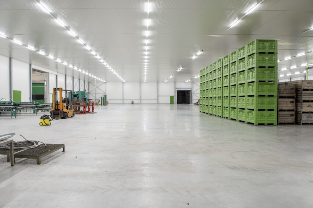Grote lege opslagruimte met groene kratten en heftruck.