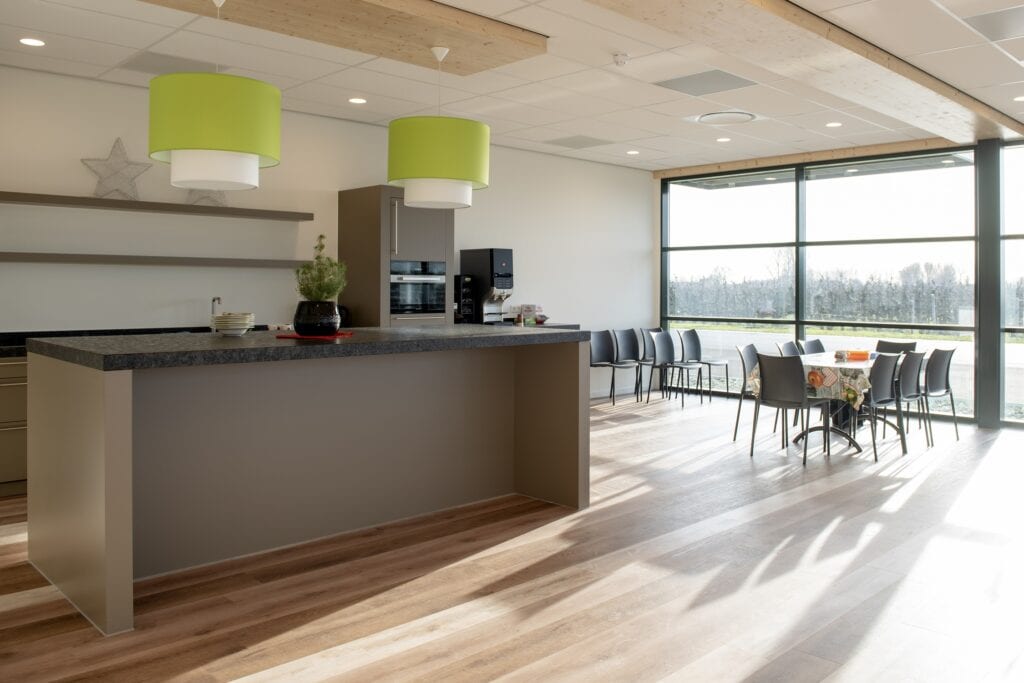 Lichte moderne ruimte met grote ramen, eettafel en groene hanglampen.