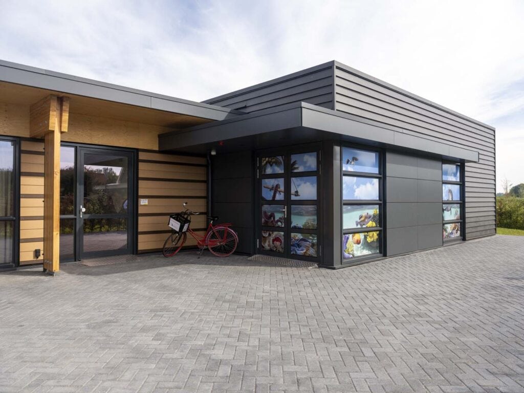 Moderne bedrijfsgebouw met grote glasramen, houten accenten en strakke architectuur, gebouwd door JC.