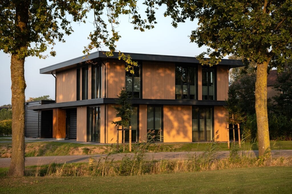 Moderne houten woning met grote ramen en strakke architectuur, omgeven door groen en bomen.