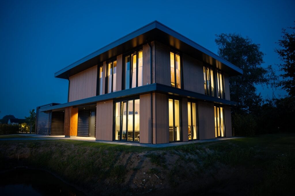 Moderne houten woning met grote ramen en verlichting, gebouwd door JCVANKESSEL BOUW.