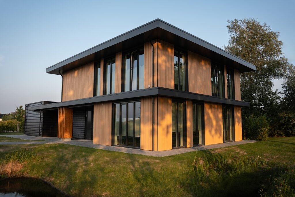 Moderne houten woning met grote ramen en strakke architectuur in een groene omgeving.