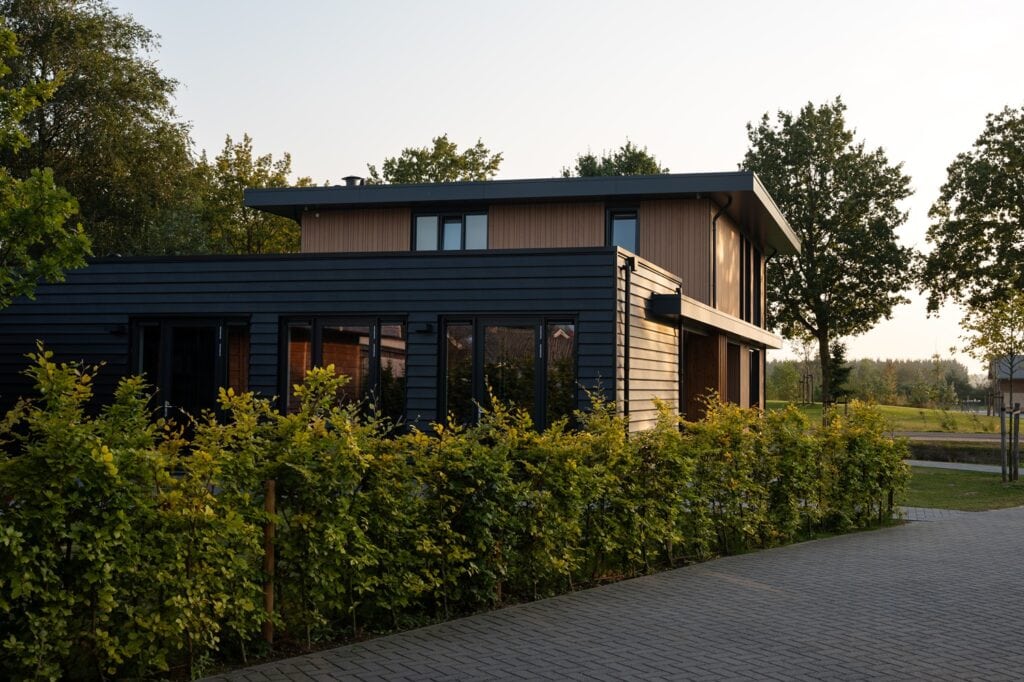 Moderne houten woning met grote ramen en groene tuin, gebouwd door JCVANKESSEL BOUW.