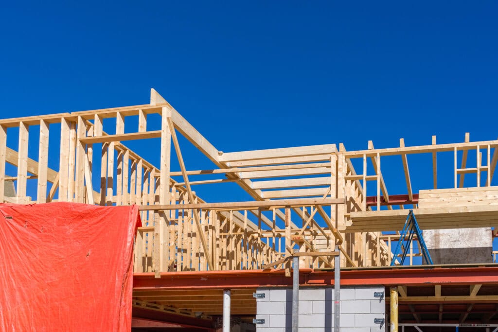 Houten bouwconstructie in opbouw met houten geraamte en blauwe lucht.