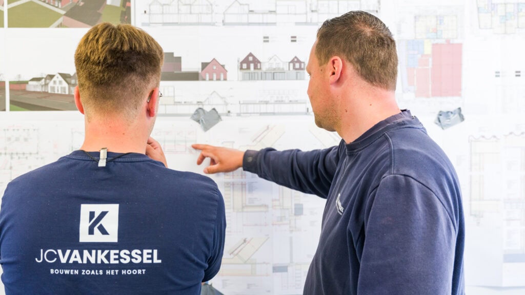 Twee bouwprofessionals bespreken bouwplannen op een bouwtekening.
