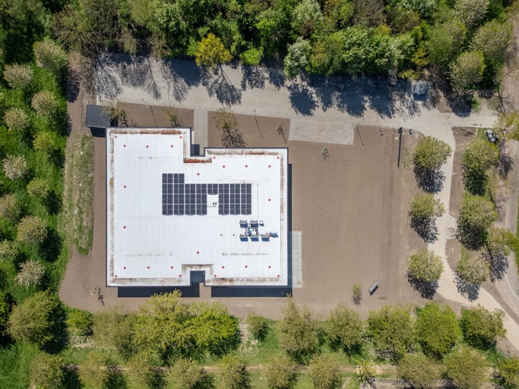 Schoolgebouw met zonnepanelen op het dak, omgeven door groen en speelplaatsen.