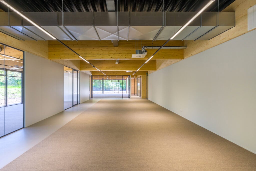 Ruime kantoorruimte met grote ramen, houten plafond en moderne afwerking.