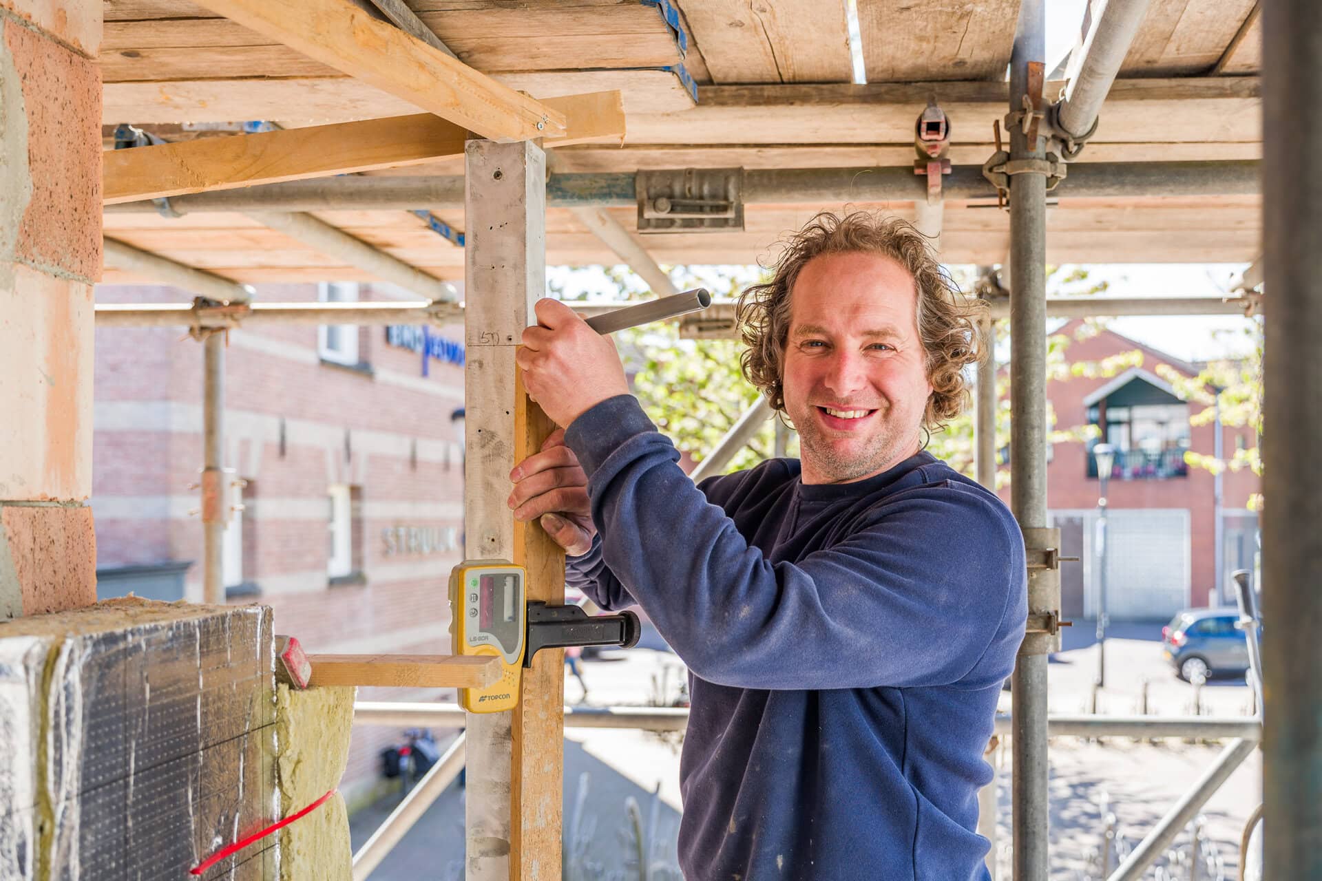 Bouwvakker bezig met constructiewerk op een bouwplaats, met houten frame en gereedschap.