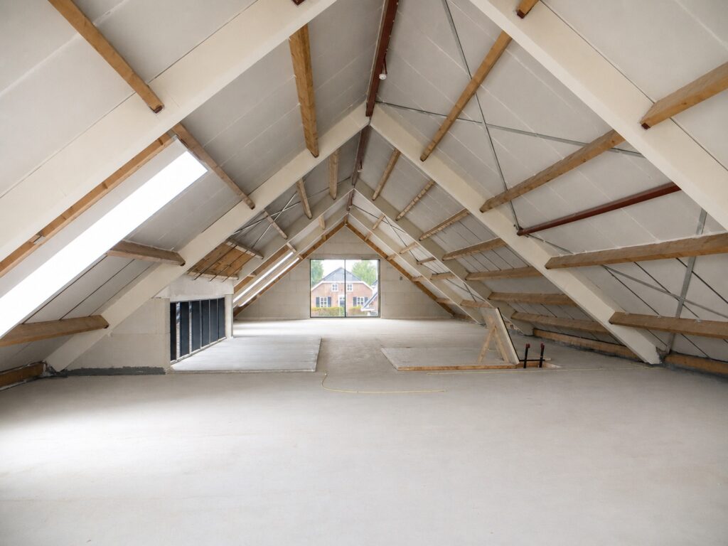 Binnenkant zolder met isolatie en houten steunbalken.