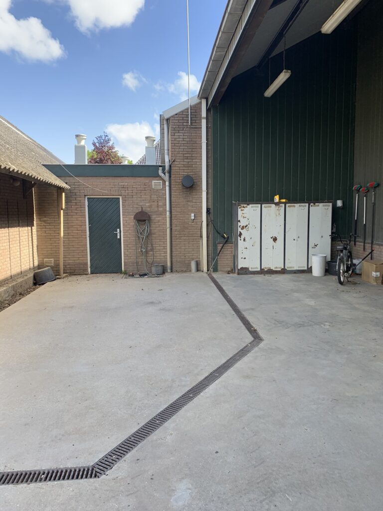 Buitenruimte met betonvloer en afwatering door drainagegoot.