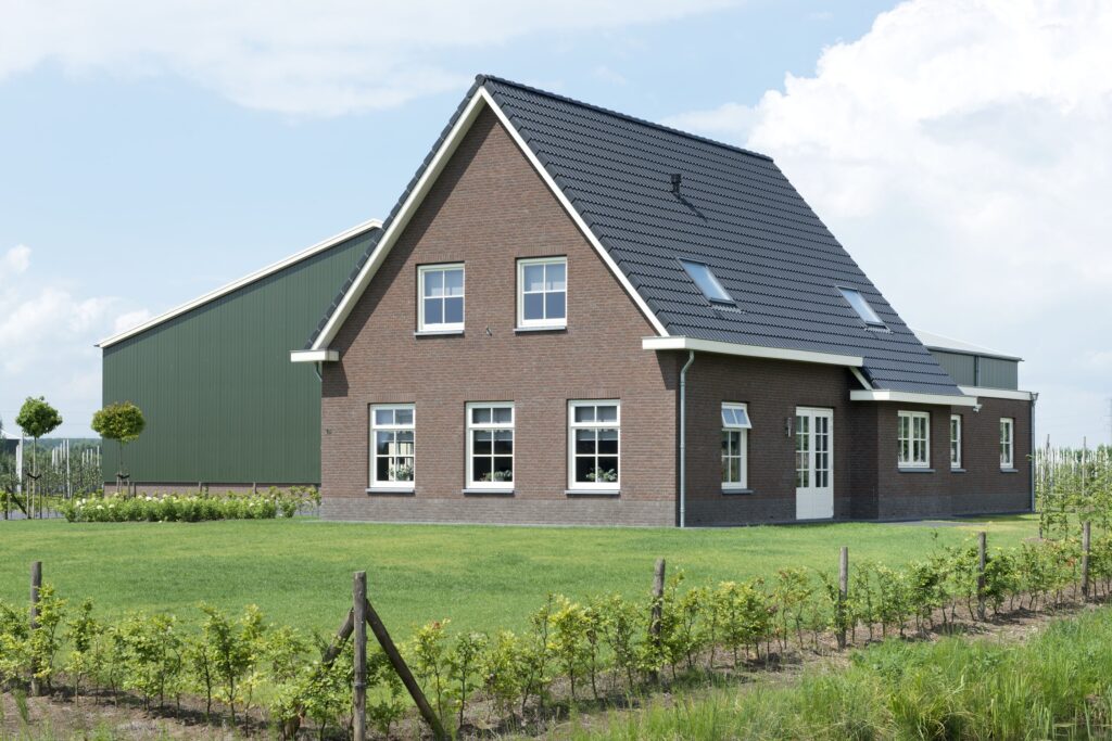 Moderne woning met tuin, schuur en zonnepanelen onder blauwe hemel.