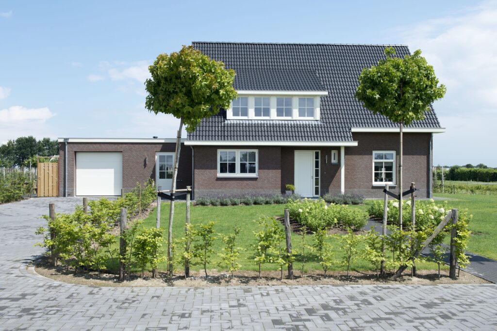 Moderne woning met tuin, bomen en oprit in landelijke omgeving.