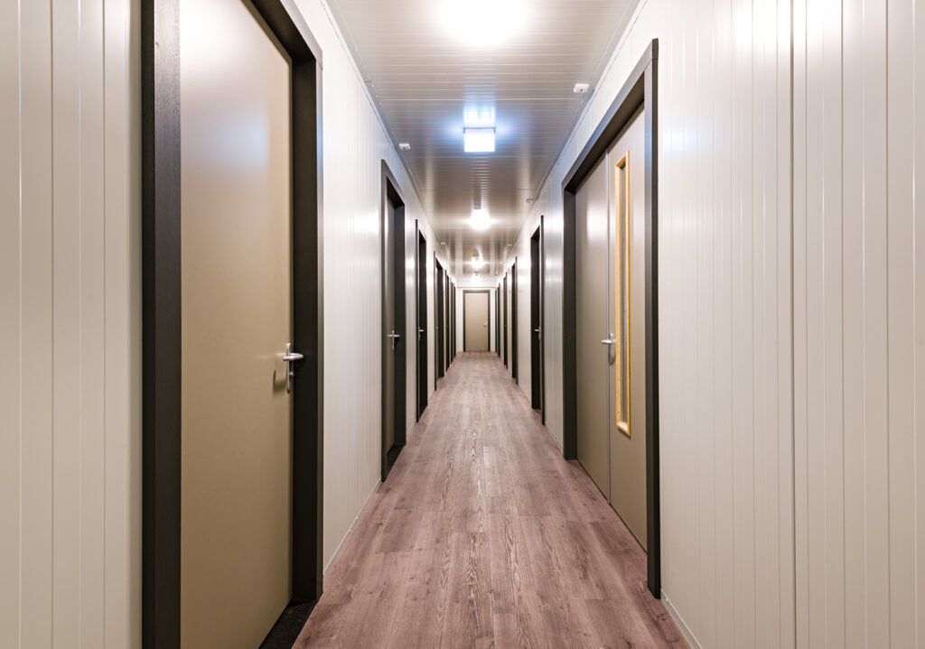 Lange hotelgang met meerdere gesloten deuren en verlichting.