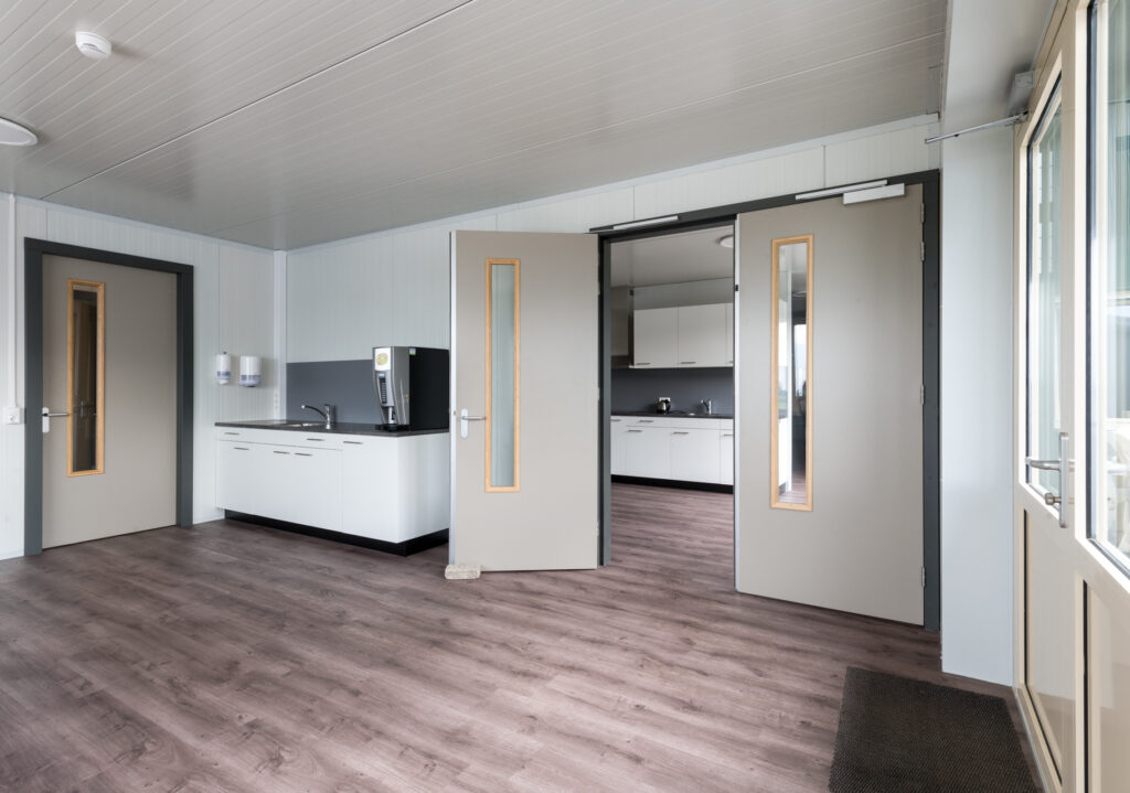 Moderne kantoorruimte met keuken en grote ramen voor natuurlijk licht.