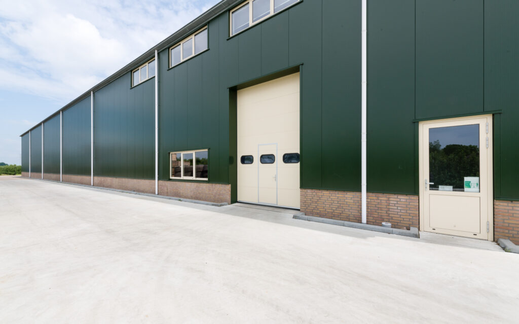 Groene industriële hal met grote deur en kleine toegangspoort.