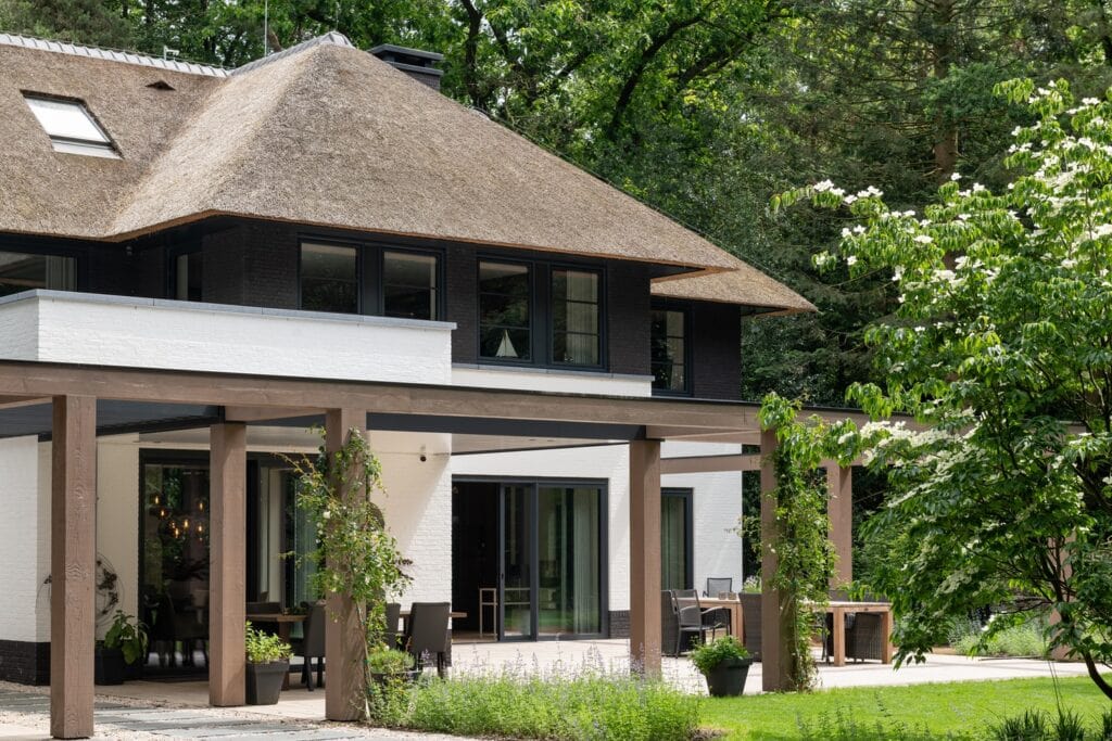 Moderne woning met natuurlijke materialen en grote ramen, omgeven door groen en bomen.