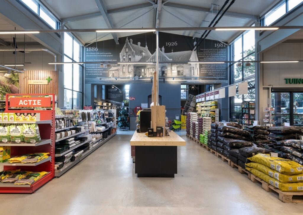 Binnenkant van een bouwmarkt met tuin- en huisdierenproducten, schappen vol zakken en tuinartikelen.