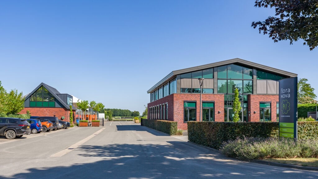 Modern bouwbedrijfgebouw met glas en bakstenen, groene omgeving en parkeerplaatsen.