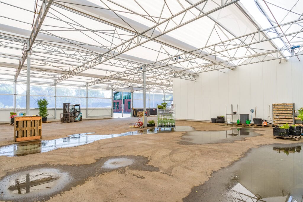 Moderne bouwtent met zand en water op de vloer, gereedschap en planten aanwezig.