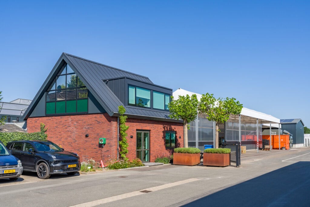 Modern bedrijfsgebouw van JCVANKESSEL BOUW met glazen gevel en groene omgeving.