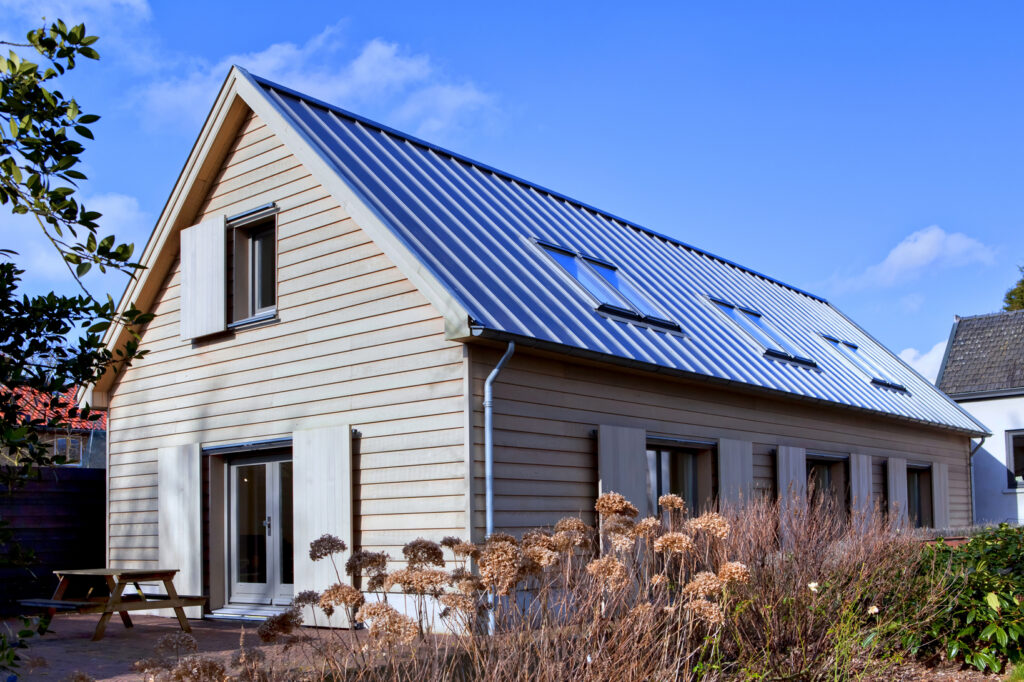 Houten huis met zonnepanelen en grote ramen onder een blauwe hemel.