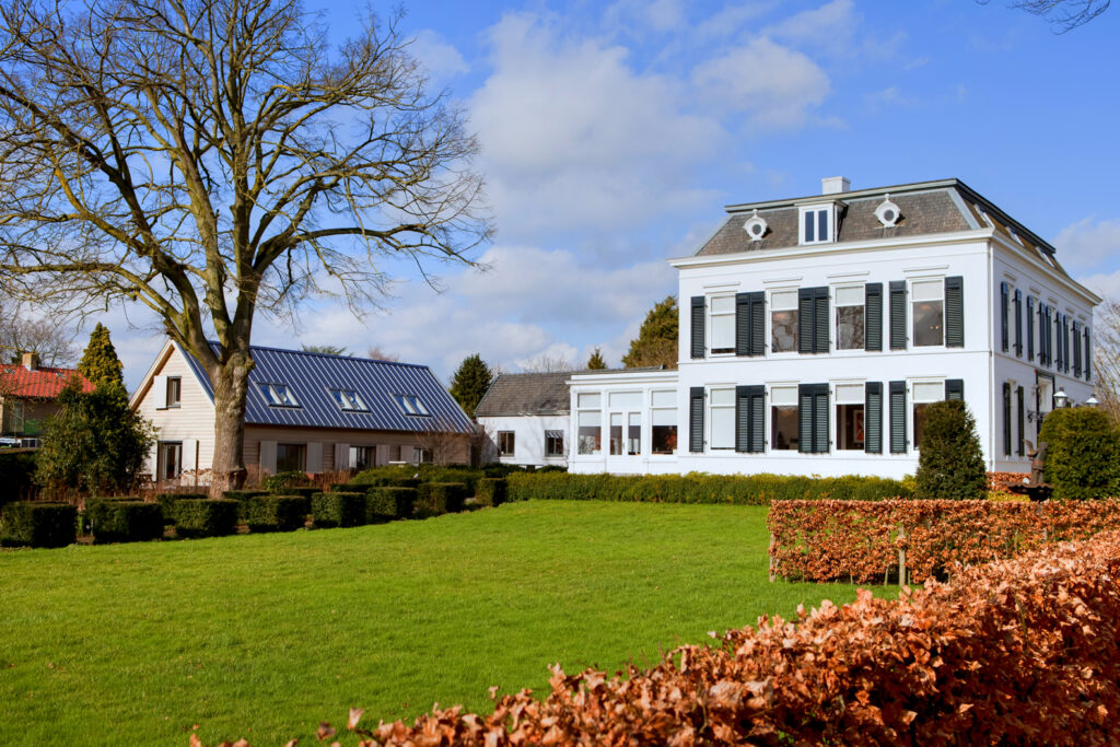 Uitzicht op een groot landhuis met witte gevel en grote ramen.