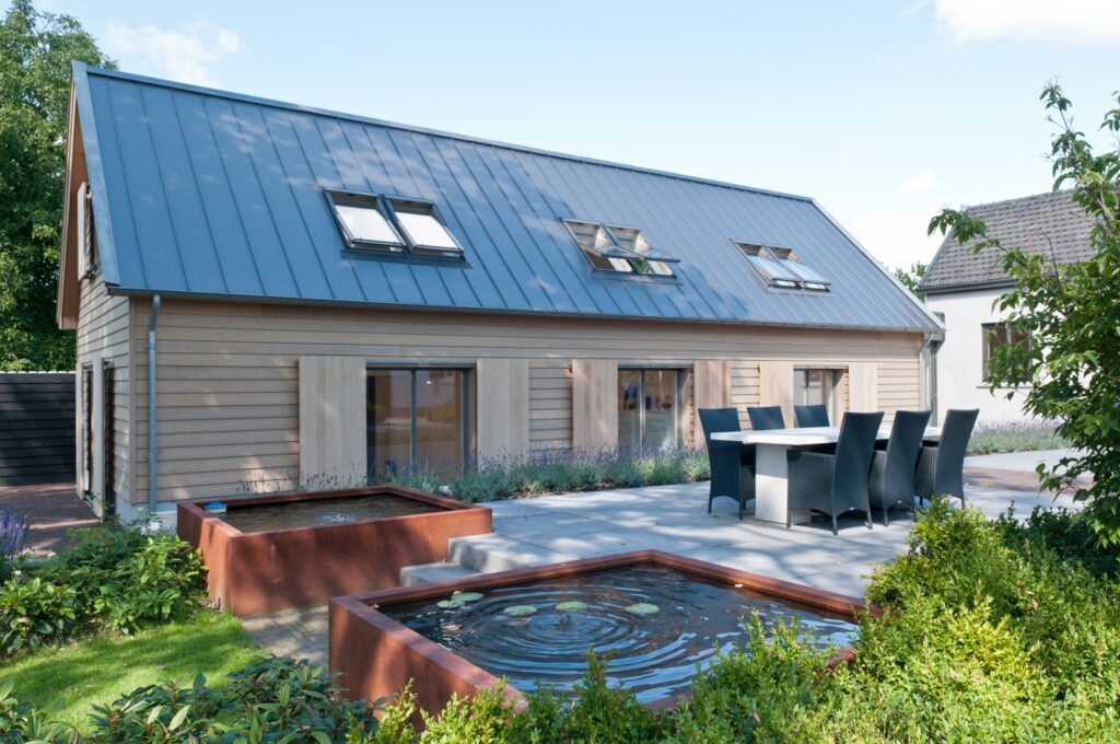 Houten woning met blauwe metalen dak, tuin en jacuzzi in de tuin.