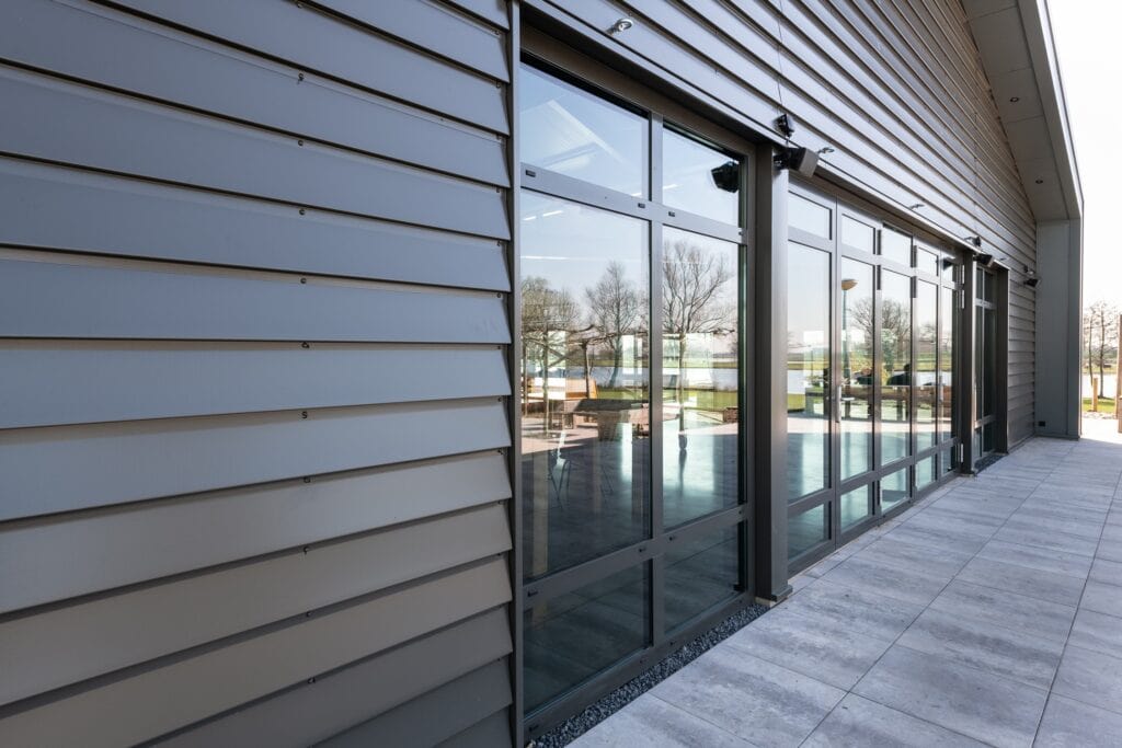 Moderne gevel met grote glazen ramen en horizontale metalen gevelbekleding.