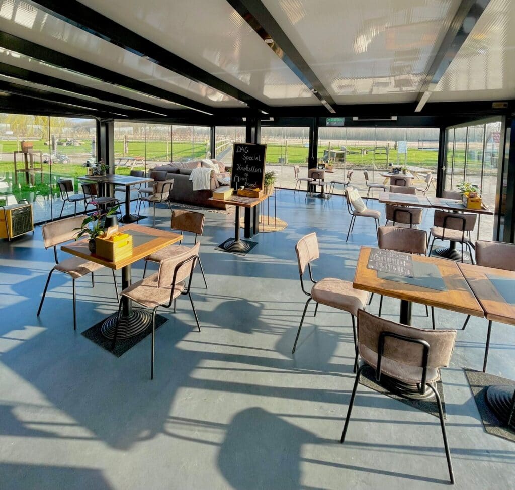 Moderne restaurant met grote ramen en uitzicht op groen landschap.
