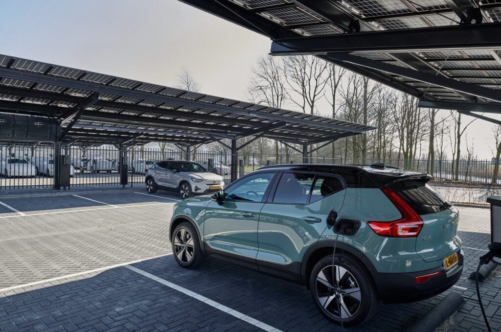 Elektrische auto opladen onder zonnepaneel overkapping.