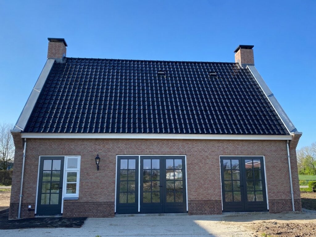 Moderne woning met grote glazen deuren en bijgebouw onder heldere blauwe hemel.