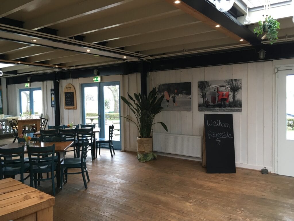 Gezellig interieur met houten vloeren, tafels en stoelen, en decoratie op de muur.
