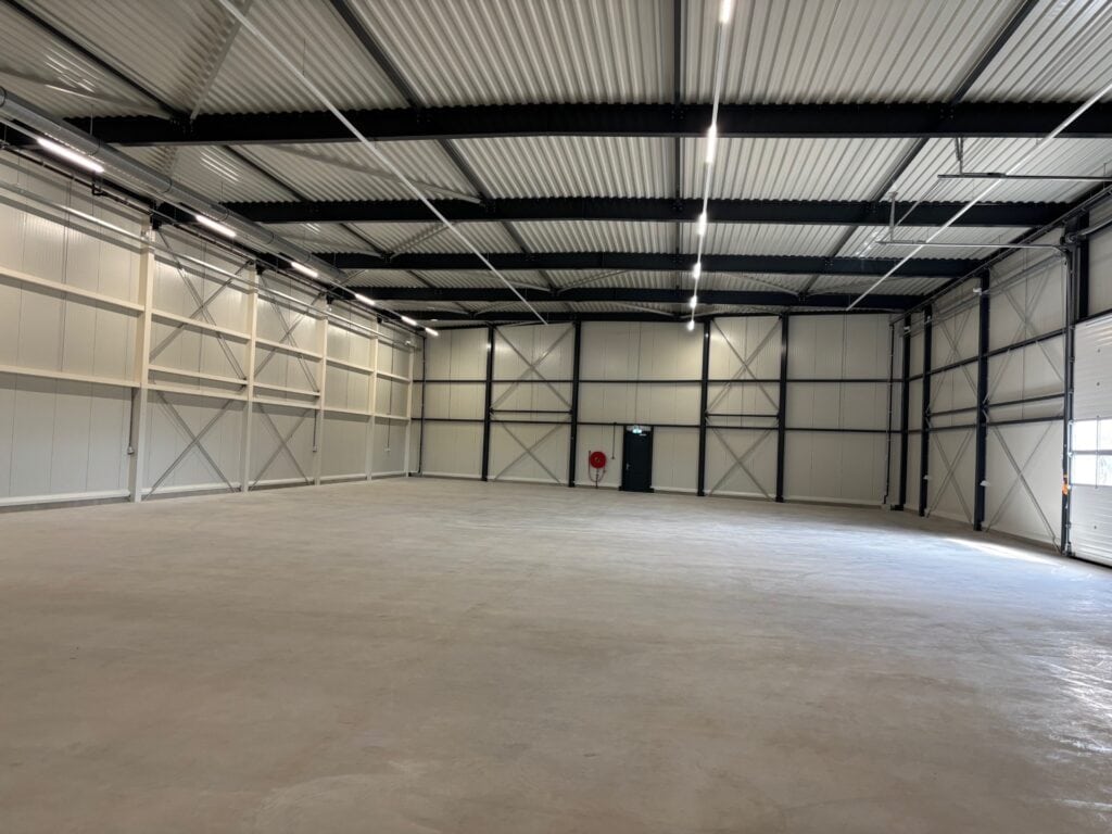 Ruime industriële hal met metalen structuur en betonnen vloer.