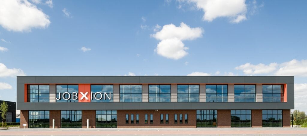 Modern kantoorgebouw van JCVANKESSEL BOUW met grote ramen en blauwe lucht.