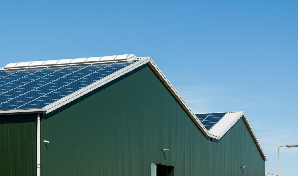 Groene bedrijfsgebouw met zonnepanelen onder een heldere blauwe hemel.