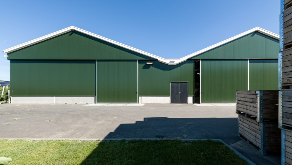 Groene bedrijfshal met schuine daklijn en open ingang.