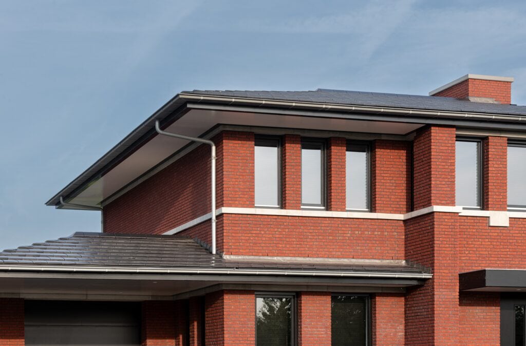 Moderne woning met rode bakstenen en grote ramen onder een dak met overstek.