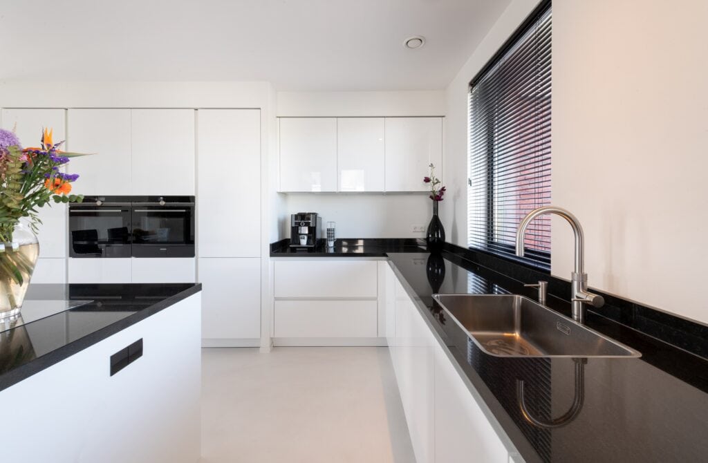 Strakke witte keuken met zwart werkblad en grote ramen in Villa Noordijk.